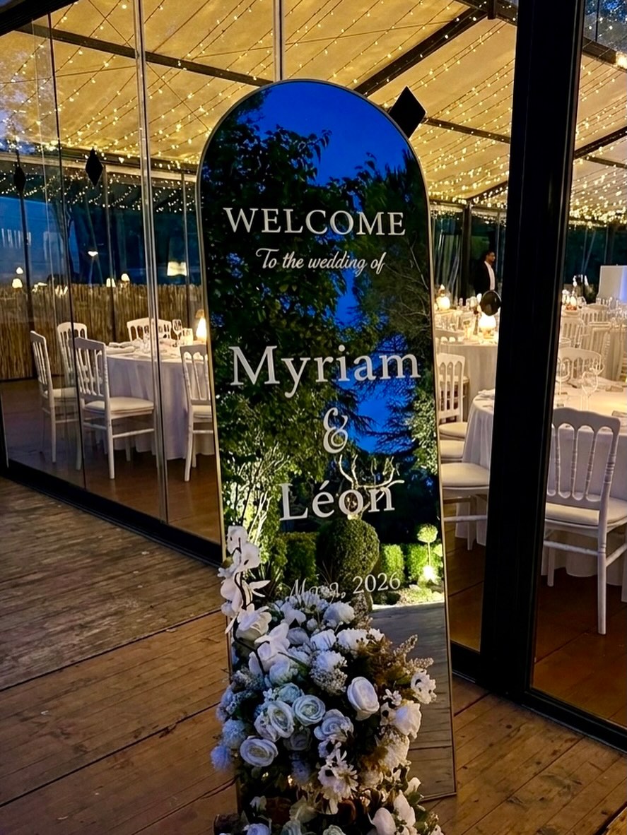 Personalised welcome mirror for a wedding, framed by white florals